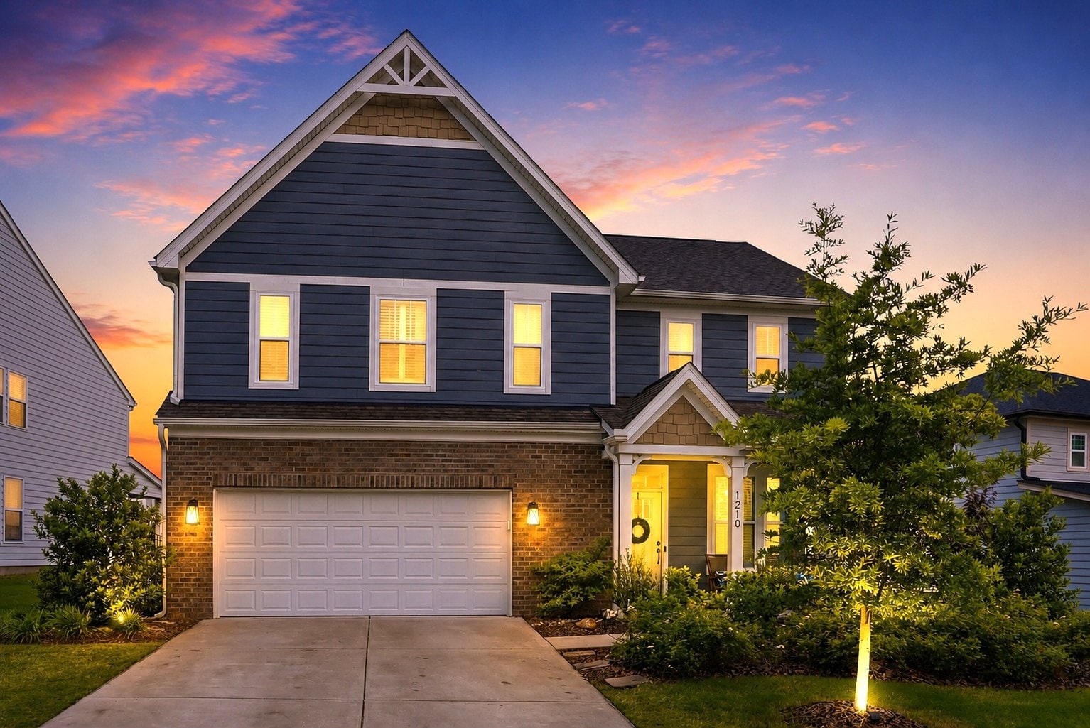 Twilight exterior of 1210 Therns Ferry Drive — a navy two-story home with glowing windows against a sunset sky